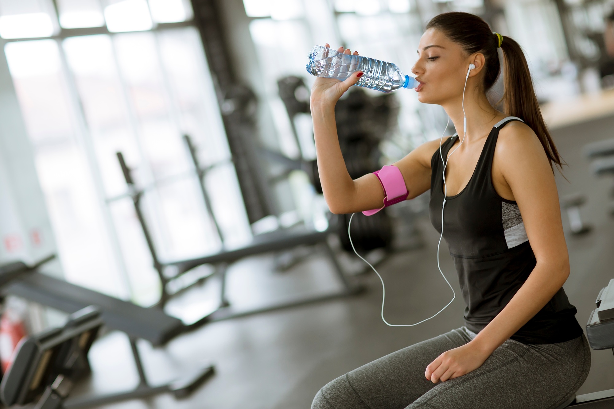 Attractive sport young woman drinking water while sitting and resting after workout