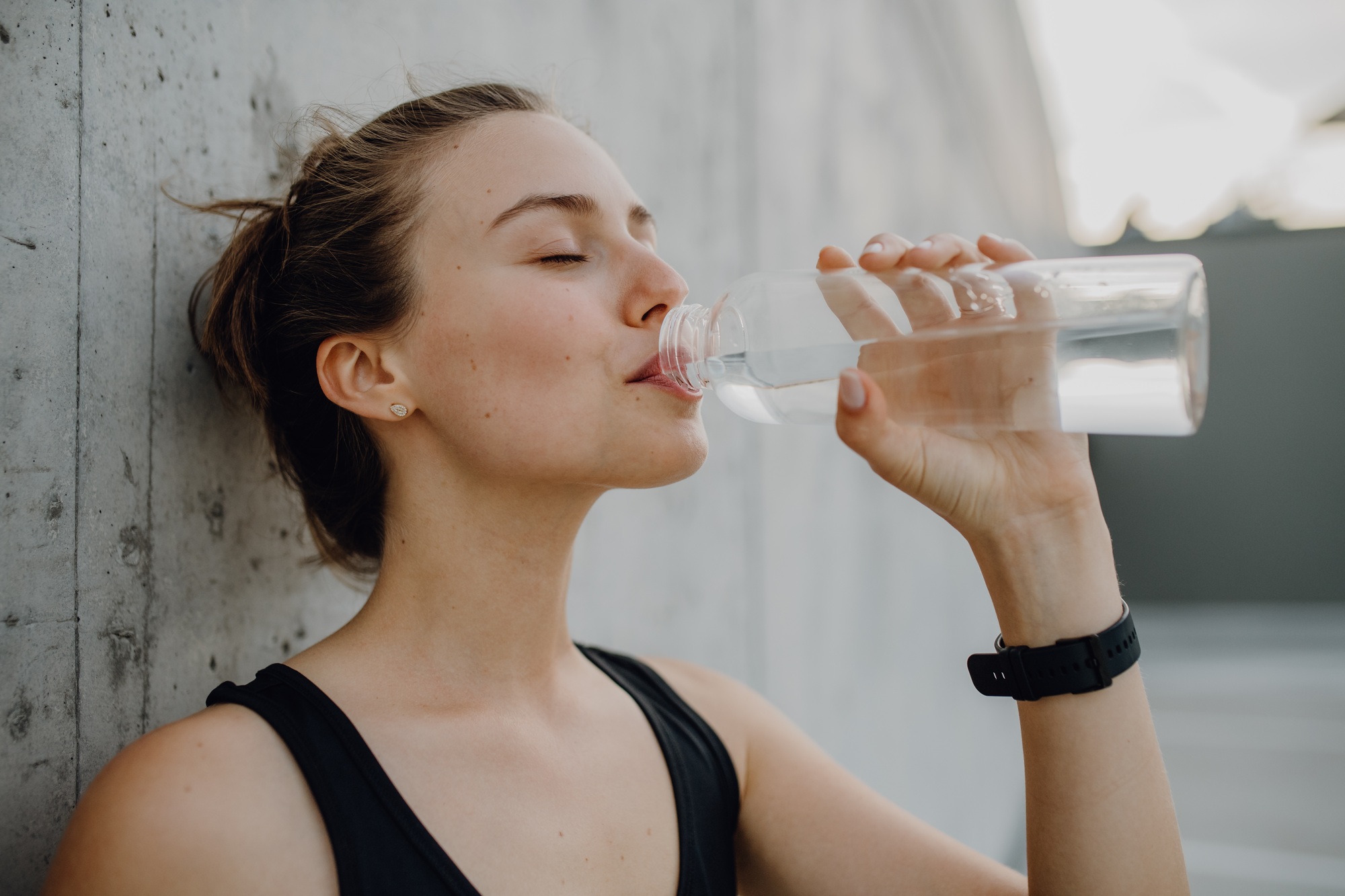 Young woman drinking water during jogging in city, healthy lifestyle and sport concept.